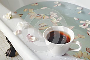 cup of tea near a clawfoot tub with petals floating in bath water