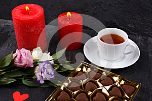 A cup of tea next to a box of chocolates and a bouquet of roses on a stone background
