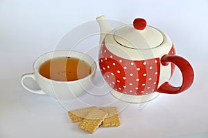 Cup of tea next to a dotted teapot and three cookies isolated on white background