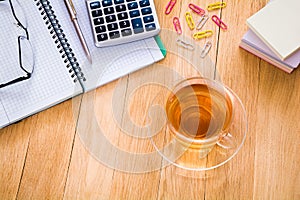 Cup of tea, notebook with pen, calculator and glasses on the desktop. Business concept