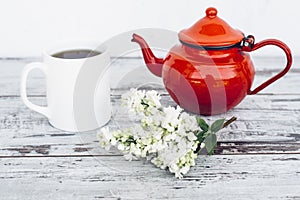 Cup of tea and old red teapot on vintage wooden table with branch of lilac