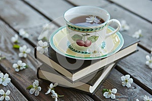 A cup of tea on a pile of books covered with cherry flowers