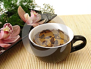 Cup of tea with pink orchids on black plate over straw matt photo