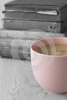 Cup of tea in a pink cup on a stack of old antique books with selective colour