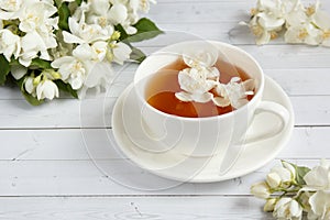 Cup of tea, pouring honey from a spoon in a jar, Jasmine flowers on a light wooden background. Copy space