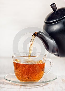 Cup of tea with pouring tea and black teapot