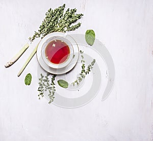 Cup of tea on a saucer with a set of herbal tea thyme, mint, lemon grass on wooden rustic background top view with text area, vint