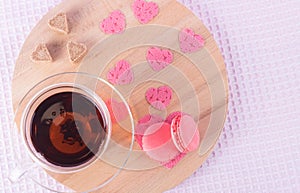 A cup of tea and a saucer with strawberry cookies along with sugar hearts and pink hearts on a light round wooden tray