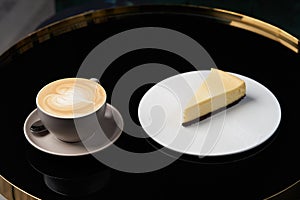 Cup of tea and slice of cheesecake on white plate on table