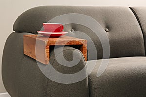 Cup of tea on sofa with wooden armrest table in room. Interior element