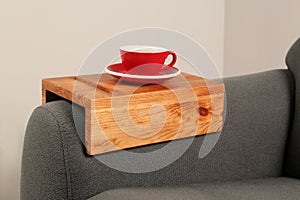 Cup of tea on sofa with wooden armrest table in room. Interior element