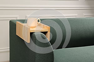 Cup of tea on sofa with wooden armrest table in room, space for text. Interior element