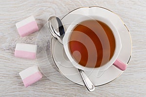 Cup of tea, spoon on saucer, pink marshmallows on table