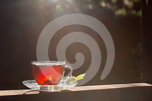 A cup of tea stands on a wooden table. Sun rays and bokeh. Dark background. Sunny summer evening, sunset