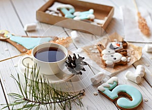 A cup of tea, sticks with sugar cristals, marshmallows and some elements of Christmas decor on a white wooden surface