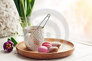 A cup of tea, sweet dessert macarons and purple tulips on a window sill.