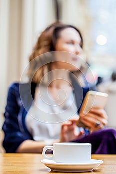 Cup of tea on the table and a woman with a smartphone in the blur zone