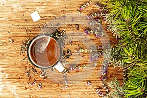 Cup of tea with tea bag in it and herbs on wooden table from above flatlay