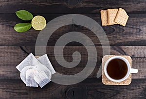 Cup of tea with tea cookies, lime and tea bags on wooden table