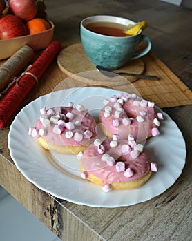 Cup of tea and three donuts with pink icing on a white plate.