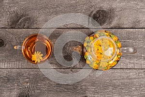 Cup of tea and transparent teapot with calendula flowers on wood background. Calendula Tea Benefits Your Health concept