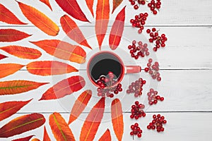 A cup of tea with viburnum berries and red autumn leaves on a wooden boards, October mood, rustic composition, colorful creative