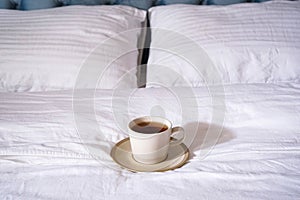 A cup of tea on a white bed, close-up. Morning concept. Decorating and furniture in a modern bedroom