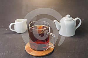 Cup of tea on wooden support, teapot and creamer on black table/cup of tea on wooden support, white teapot and creamer on black