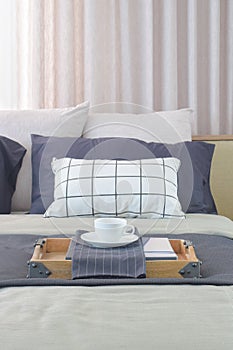 Cup of tea and wooden tray setting on bed with classic color scheme bedding