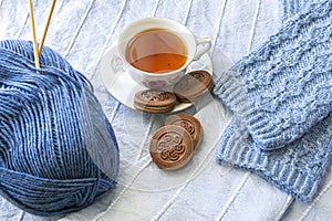 Cup of tee with chocolate cookies, knitted socks and ball of yarn with knitting needles