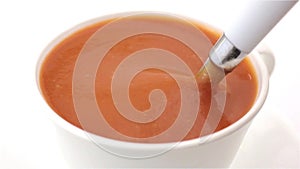 A cup of tomato soup being stirred
