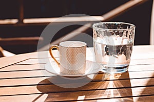 A cup of Turkish coffee and a glass of water on the wooden table on a terrace in a garden, coffee break