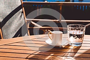 A cup of Turkish coffee and a glass of water on the wooden table on a terrace in a garden, coffee break