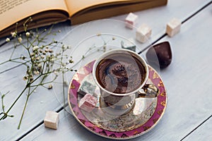 Cup of Turkish coffee with Turkish delights and heart shaped chocolate next to the old book