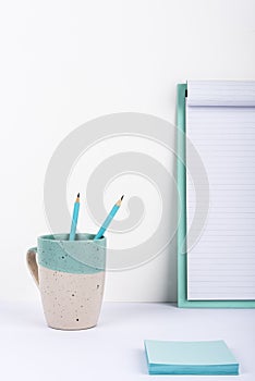 Cup With Two Pencils Inside Placed On Office Desk With Clipboard With Important Message And Notes. Mug With Pens On