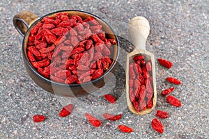 Cup and wooden spoon with dried red goji berries on gray stone background