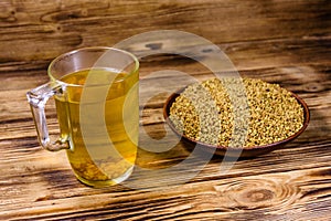 Cup of yellow tea methi dana and plate with fenugreek seeds on wooden table