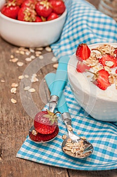 In a cup of yogurt, oat granola and fresh strawberries, on a blu