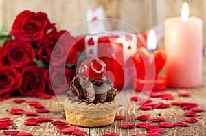 Cupcake with cherry in front of bouquet of red roses