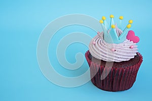 Cupcake with crown and pink heart over blue background