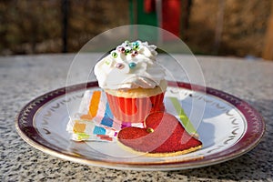 Cupcake or cup cake with whipped cream and small colorfull sugar perils served on the small dessert plate with paper napkin and re photo