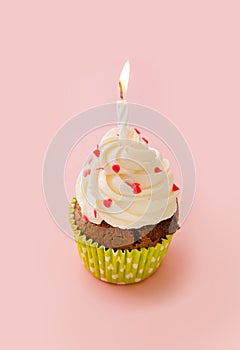 Cupcake decorated with cream and decorative hearting on a pink b