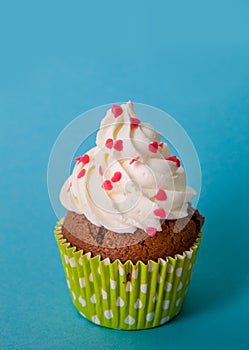 Cupcake decorated with whipped cream and decorative hearting on a blue background