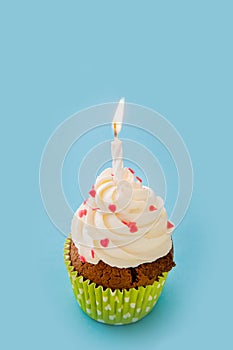 Cupcake decorated with whipped cream and decorative hearting on a blue background