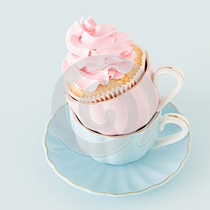 Cupcake with gentle pink cream decoration in two cups on blue pastel background.