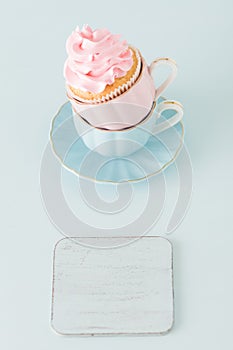 Cupcake with gentle pink cream decoration in two cups on blue pastel background.