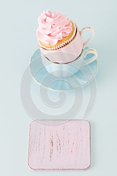 Cupcake with gentle pink cream decoration in two cups on blue pastel background.
