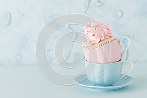 Cupcake with gentle pink cream decoration in two cups on blue pastel background.