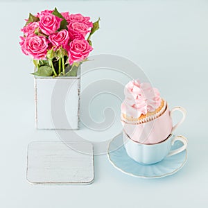 Cupcake with gentle pink cream decoration in two cups on blue pastel background.