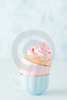 Cupcake with gentle pink cream decoration in two cups on blue pastel background.